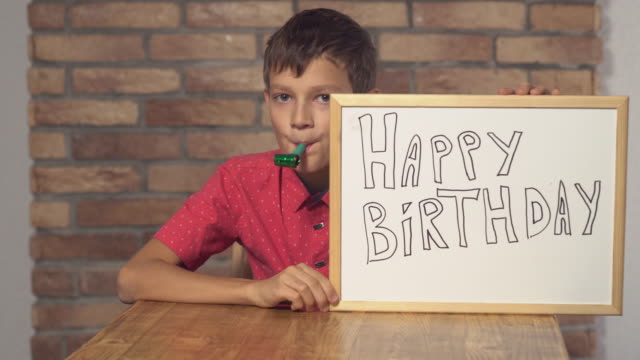 Kind-am-Schreibtisch-hält-Flipchart-mit-Schriftzug-Herzlichen-Glückwunsch-zum-Geburtstag-auf-dem-Hintergrund-roten-Backsteinmauer