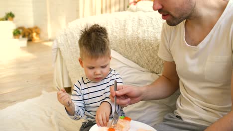Little-adorable-boy-celebrating-his-birthday-with-young-father-eat-cake-in-bedroom