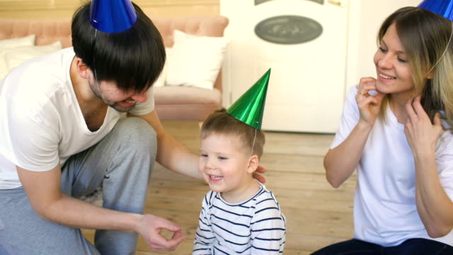 Father-of-happy-family-celebrating-birthday-dress-hat-to-son-at-home