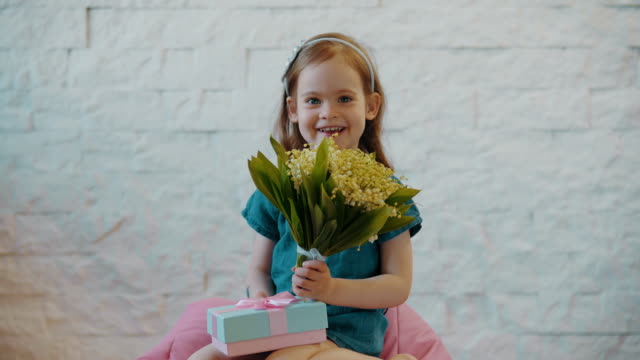 niedliche-kleine-Mädchen-zeigt-Blumen-und-ein-Geschenk