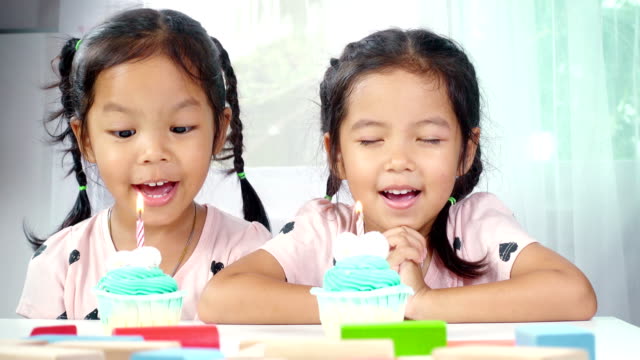 Zwei-asiatische-Mädchen-bläst-Kerzen-auf-Geburtstagskuchen-zusammen-im-Haus