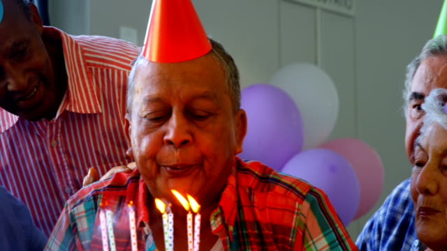 Senior-hombre-soplando-las-velas-de-un-pastel-de-cumpleaños-con-sus-amigos-4k