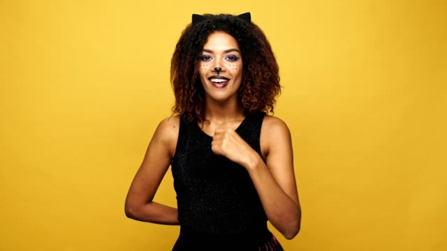 Gato-joven-mujer-africana-con-maquillaje-bonito-llamando-y-dando-presente-aislado-sobre-amarillo