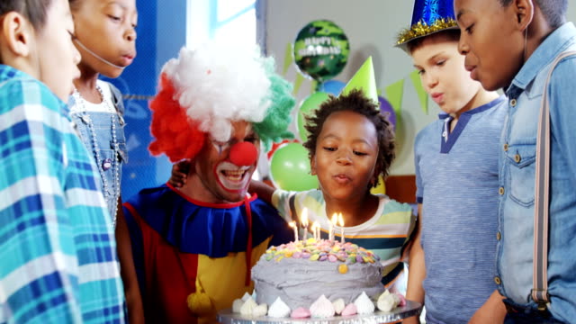 Los-niños-con-el-payaso-soplando-velas-sobre-el-pastel-durante-cumpleaños-partido-4k