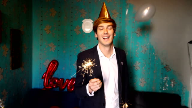 Young-adult-man-enjoy-new-year-eve-birthday-party-dancing-with-sparkler-in-cozy-home-indoor