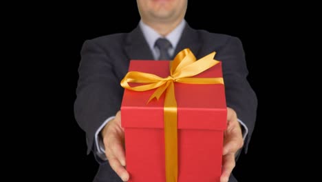 A-man-in-a-business-suit-with-a-tie-is-holding-a-red-gift-box.-A-man-gives-a-gift.-A-businessman-with-a-gift-in-his-hands.-Green-screen-alpha-channel-transparent-background.-From-unfocus-to-focus.