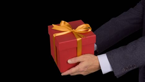 Two-male-hands-holds-red-gift-box-with-gold-bow.-Celebrate-eve-present-gift-box.-Caucasian-man-in-classical-suit.-Alpha-channel-chroma-key-transparent-background.-Locked-down.