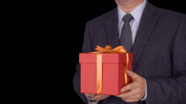 Caucasian-businessman-hold-and-give-red-gift-box.-From-unfocus-to-focus-motion.-Adult-man-in-classic-business-suit-hold-red-gift-box.-Alpha-channel-chroma-key-transparent-background.-Locked-down.