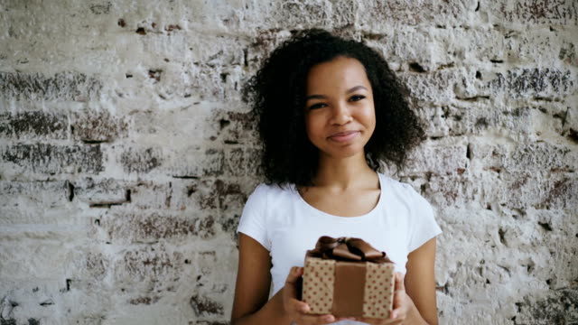 Portrait-of-young-african-american-woman-holding-gift-box-and-smiling-into-camera