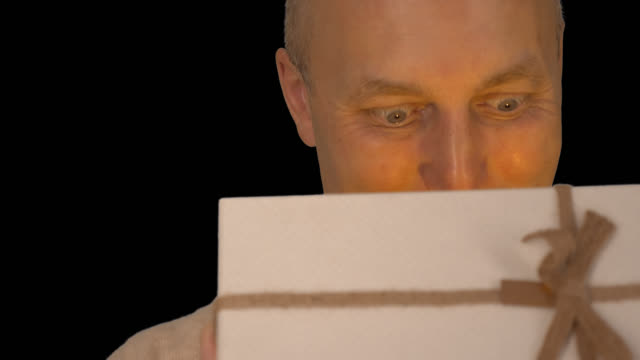 Adult-caucasian-man-open-gift-box.-Extreme-close-up.-Man-looking-to-gift-box-and-speaking.-A-man-really-likes-the-gift.-Beige-sweater.-Alpha-channel-chroma-key-transparent-background.