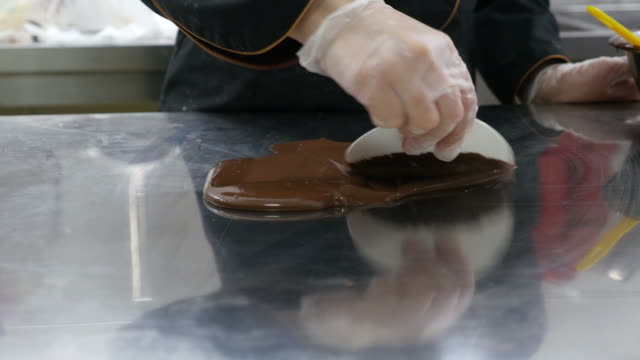 Ein-Konditor-Verbreitung-Schokoladenglasur-auf-einem-Tisch-um-Schokoladendekorationen-zu-machen