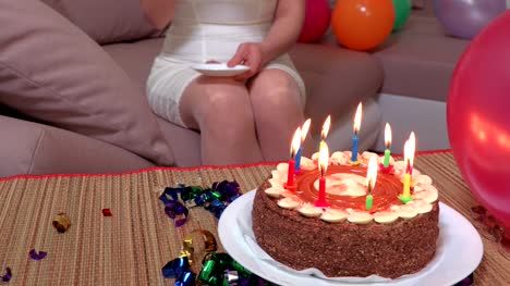 Woman-with-cup-of-coffee-sitting-on-sofa-near-birthday-party-cake-with-burning-candles