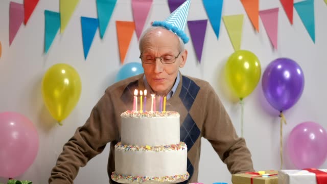 Fröhliche-Senioren-bläst-Kerzen-auf-einem-Geburtstag-Kuchen-und-seine-Daumen-hochhalten