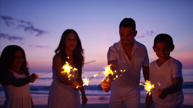 Hispanic-family-celebrating-birthday-with-sparklers-on-beach