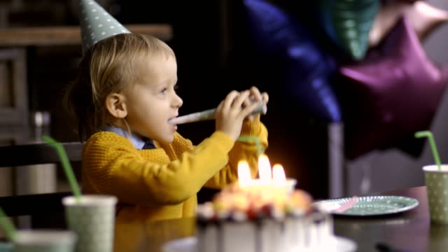 Cute-toddler-boy-blowing-birthday-horn-at-table