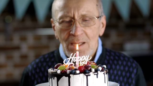 Close-up-of-senior-man-blowing-candle-on-cake