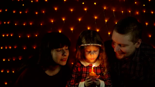 Ein-kleines-Mädchen-bläst-eine-Kerze-auf-eine-festliche-Torte-mit-ihrer-Mama-und-Papa.