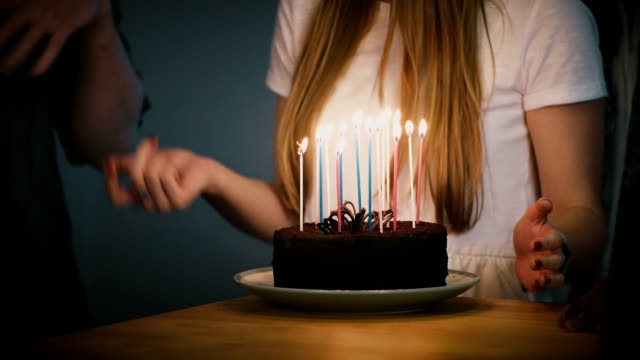People-dancing-around-birthday-cake-with-candles.-Friends-celebrate-together.-Girl-in-white-shirt-holds-a-pie.-Party.-4K