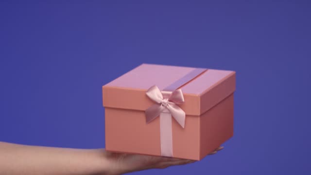 Mano-de-mujer-sosteniendo-una-caja-de-regalo-rosa-en-pantalla-azul;-Concepto-de-celebración