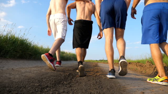 Male-friends-walking-on-country-road-and-having-fun.-Group-of-happy-boys-fool-around-outdoors.-Rear-back-view-Low-angle-view-Close-up