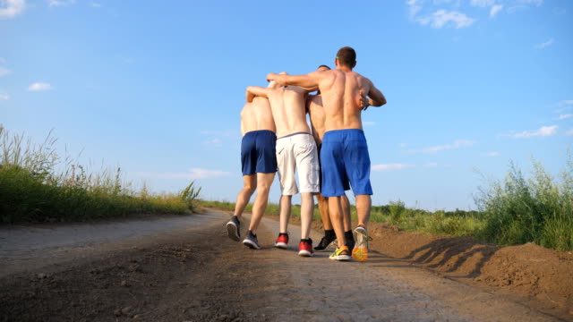 Male-friends-walking-on-country-road-and-having-fun.-Group-of-happy-boys-fool-around-outdoors.-Rear-back-view-Low-angle-view-Close-up