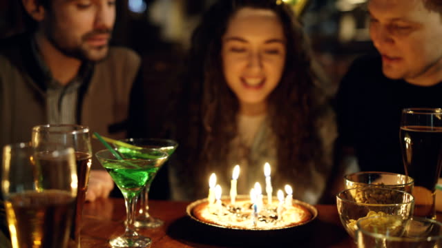 Close-up-shot-of-young-pretty-woman-blowing-out-candles-on-birthday-cake.-Happy-people-are-laughing-and-clapping-hands.
