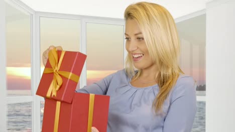 Woman-receiving-gift-in-red-box-on-window-background-with-evening-sunset-in-sea