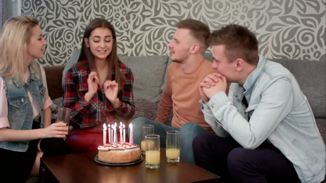 Chica-adolescente-atractiva-celebra-su-cumpleaños-con-amigos-en-casa-y-sopla-las-velas-sobre-el-pastel-y-bebidas-jugo-naranja