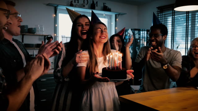 Happy-Caucasian-girl-holding-birthday-cake,-making-a-wish-at-cheerful-fun-multiethnic-party-with-friends-slow-motion-4K