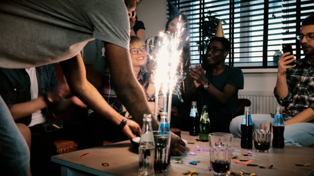 Multiethnische-Freunde-gratulieren-kaukasischen-schüchtern-Geburtstagskind-mit-funkelnden-Feuerwerk-Kuchen-bei-Überraschung-Partei-Slow-motion
