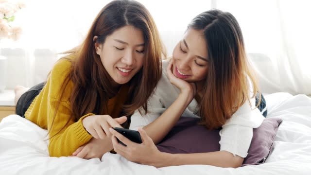 Joven-pareja-lesbiana-asiática-usando-app-smartphone-en-camas-en-su-casa.