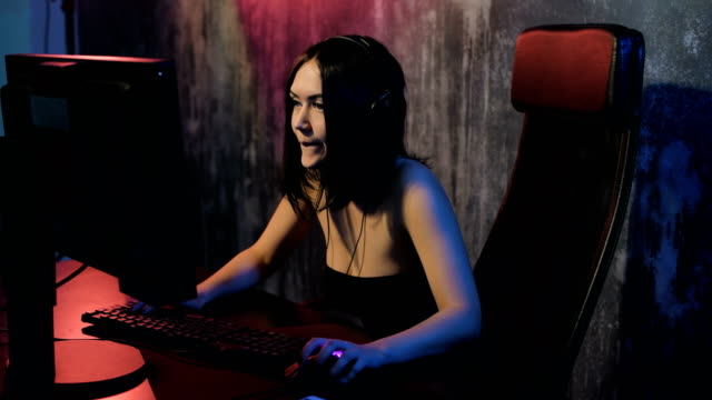 Serious-woman-enjoys-victory-in-a-video-game.-Gamer-girl-playing-online-game-on-a-pc-computer-wearing-headset-and-talking-with-a-team-using-microphone