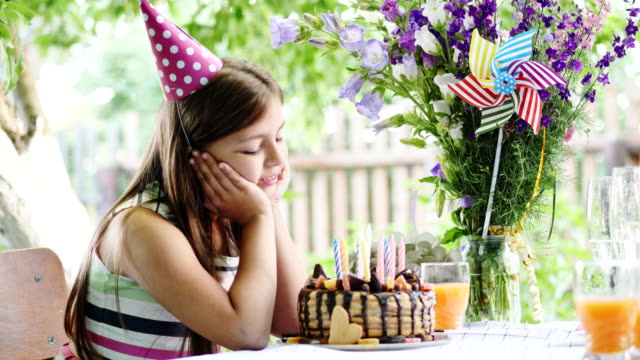 Glückliches-Mädchen-am-Tisch-im-Garten-sitzen-und-bewundert-eine-festliche-Torte