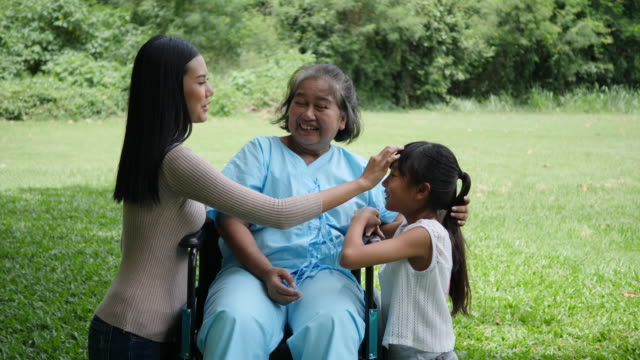 Grandmother-sitting-on-wheelchair-with-daughter-and-granddaughter-enjoy-in-the-park-together
