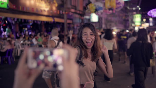 Reisender-nimmt-Backpacker-Blogger-asiatische-Frauen-Lesben-LGBT-Paar-mit-Smartphone-Fotos-in-Thailand.-Weiblich,-trinken-Alkohol-oder-Bier-an-der-Khao-San-Road-die-berühmteste-Straße-in-Bangkok.