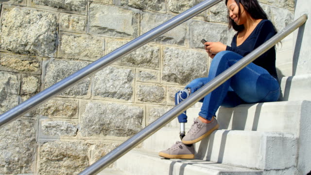 Side-view-of-disabled-woman-texting-on-mobile-phone-at-stairs-4k