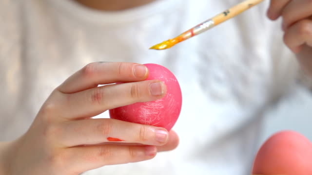 Little-kid-using-brush-with-yellow-paint-to-decorate-dyed-Easter-egg,-creativity