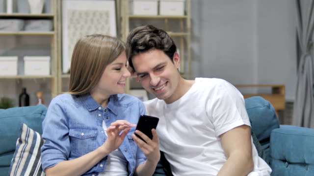 Glückliches-junges-Paar-zu-Hause-Surfen-Internet-auf-Smartphone