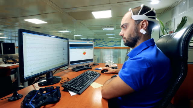 Männliche-Ingenieur-Kontrollen-Computer-mit-speziellen-Brainwave-Scannen-Kopfhörer