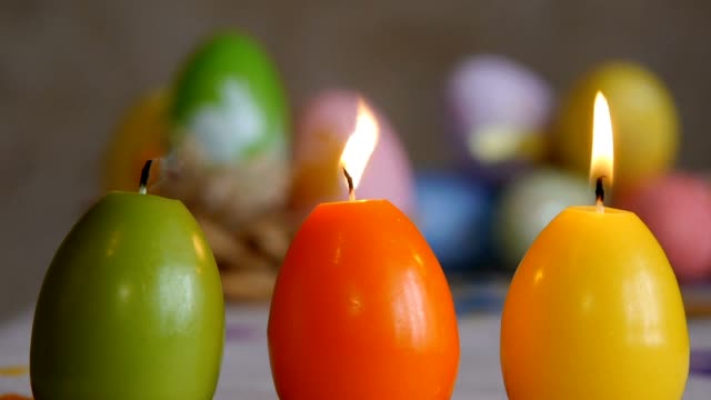 Kerzen-in-Form-von-Osterei.-Brennende-Kerzen.-Grün,-orange,-gelb.-Ostereier-Kerzen-und-bunte-Ostereier-im-Hintergrund.