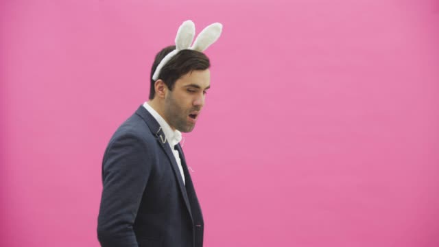 Young-charismatic-couple-on-pink-background.-With-hackneyed-ears-on-the-head.-During-this,-the-person-pretends-to-smoke-carrots-and-looks-at-an-attractive-look-at-his-wife.