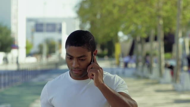 Deportista-musculoso-reflexivo-hablando-en-el-teléfono-inteligente-al-aire-libre.