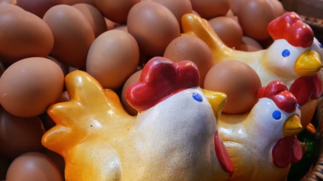 Keramikhühner-in-der-Nähe-von-Eiern.-Nahe-schöne-Keramikhühner-in-riesigen-Korb-mit-Haufen-frischer-Eier-platziert.