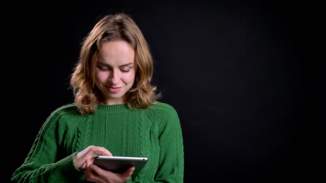 Closeup-portrait-of-adult-caucasian-female-scrolling-on-the-tablet-glancing-at-camera-and-smiling