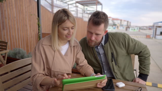 Ehepartner-diskutieren-und-prüfen-elektronischen-Katalog-in-Tablet,-sitzen-im-Café