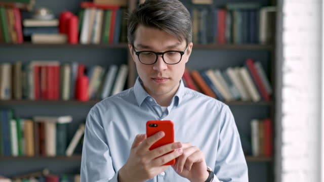 Junge-Mann-Porträt-mit-Smartphone-Lachen-stehen-in-der-Bibliothek-Social-Media-lustig