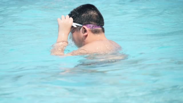 Niño-preadolescente-asiático-usando-gafas-y-jugando-en-la-piscina.