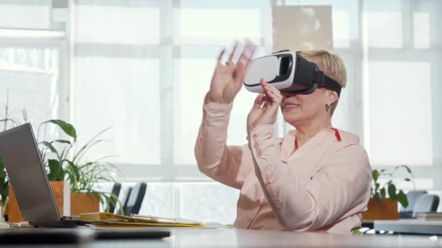 Mature-businesswoman-trying-3d-virtual-reality-glasses-at-her-workplace