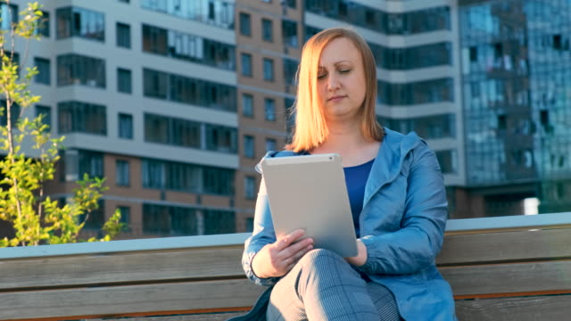 Frau-mit-Tablet-Computer-sitzt-auf-Bank-in-der-Stadt