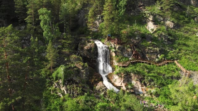 Drone-sobrevolando-un-bosque-verde-con-cascada-en-las-montañas-altai
